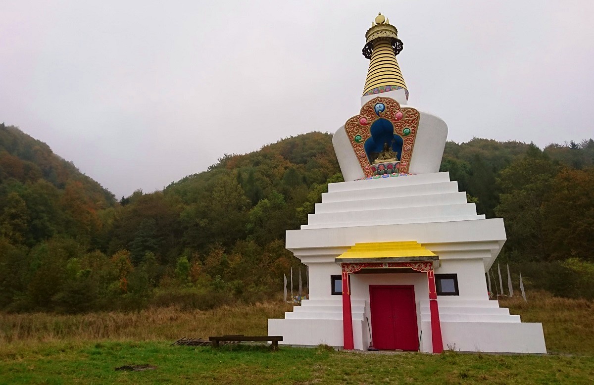 Biała stupa buddyjska ze złotym szczytem na tle lasu w Darnkowie